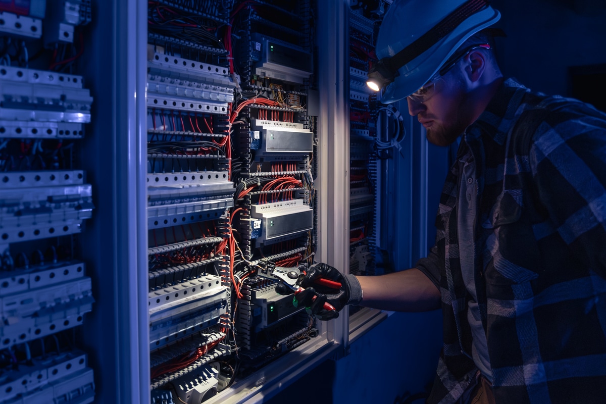 Male electrician working in switchboard with electrical connecting cable